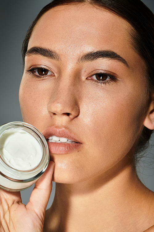 A woman gently applies a cream to enhance her natural beauty in a serene atmosphere.