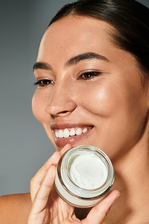 The beautiful woman smiles confidently while showcasing her skincare routine in calming light.