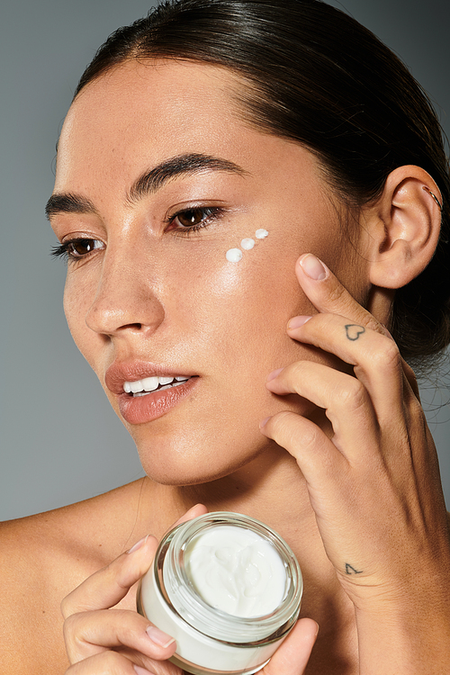 A woman gently applies cream to her face, showcasing beauty and self care in a calm atmosphere.