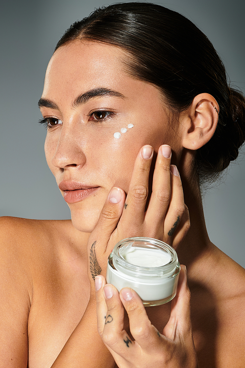 A serene moment as a woman applies skincare cream on her cheek with focus and care.