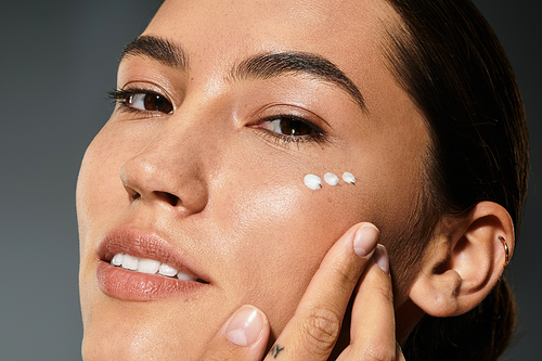 A woman gently touches her cheek while applying skincare, radiating beauty and confidence.