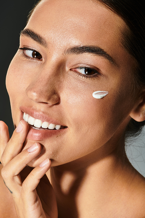 A woman with a radiant smile applies cream to her face while enjoying a moment of self care.