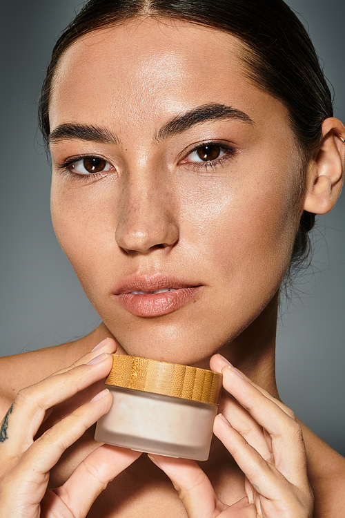 A stunning woman highlights her natural beauty while holding a skincare product elegantly.