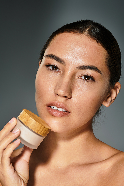 The woman gently holds a jar of cream, highlighting her radiant skin and natural beauty.