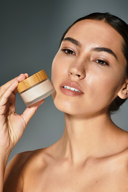 A graceful woman gently holds a skincare product near her face, embodying elegance and care.