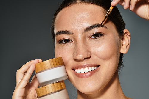 The woman showcases her radiant skin while applying a skincare product with a smile.