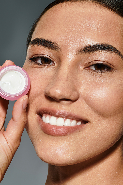 The woman smiles brightly while showcasing a skincare product, celebrating beauty rituals.