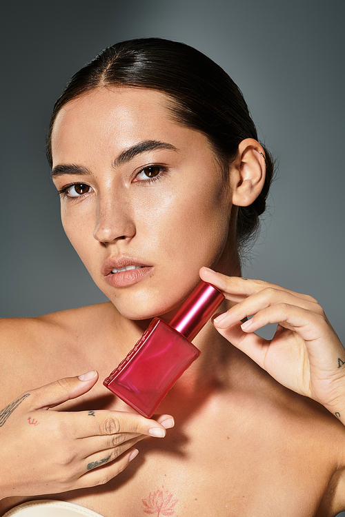 The beautiful woman elegantly presents a striking red perfume bottle against a stylish backdrop.