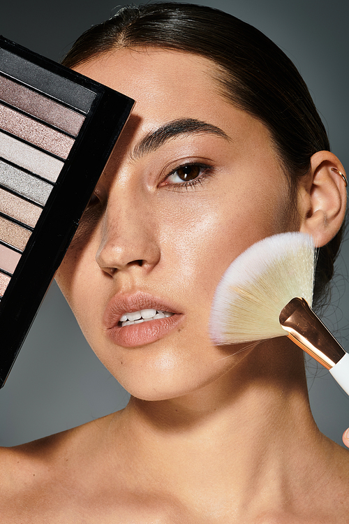 A beautiful woman enhances her features using a makeup palette and brush in a chic atmosphere.