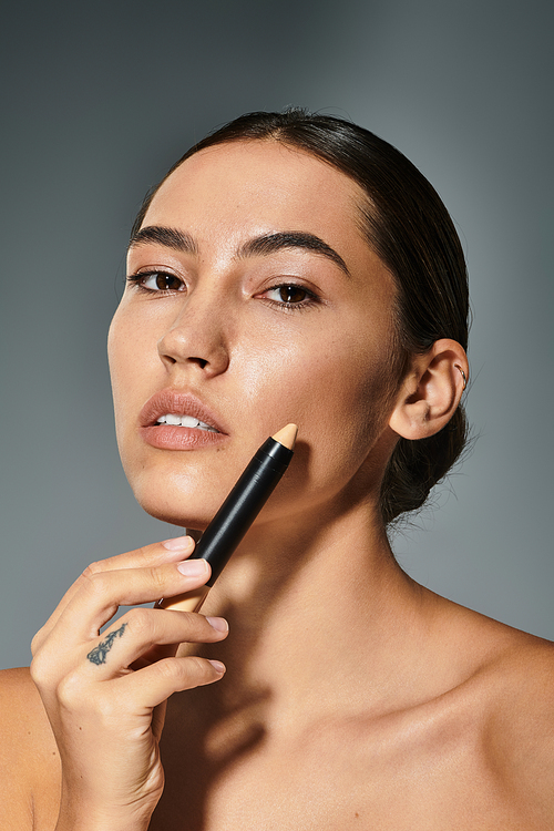 A graceful woman enhances her beauty using a makeup stick while posing confidently.