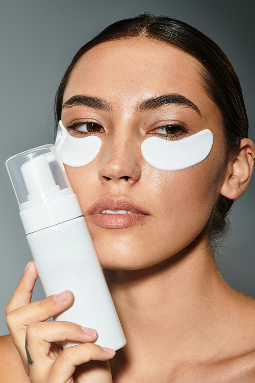 A woman enhances her skincare routine with eye patches while holding a cream bottle.