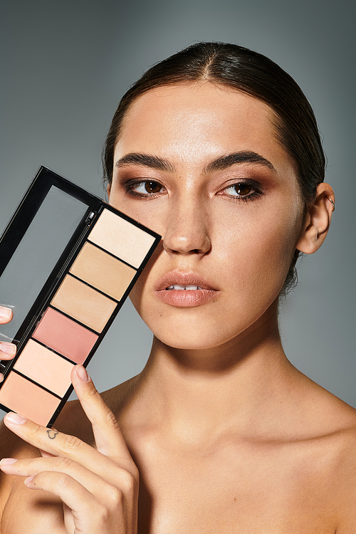 A stunning woman displays her makeup palette, highlighting her graceful features and artistry.