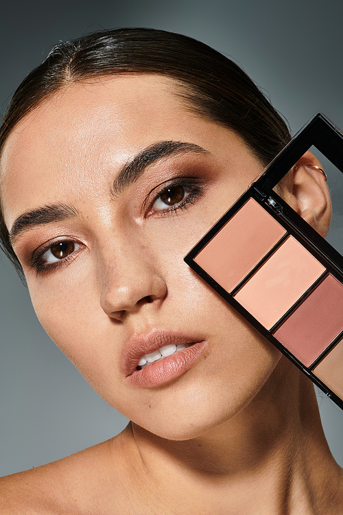 The woman displays her captivating features while holding a makeup palette.