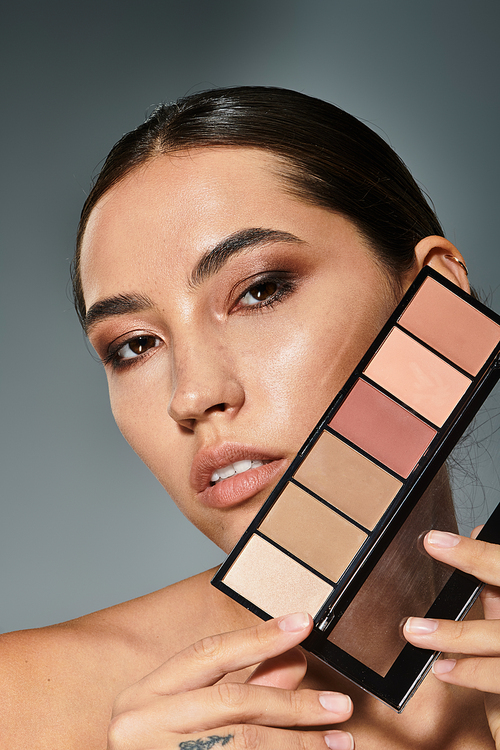 A captivating woman delicately holds a makeup palette while displaying confidence.