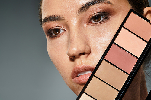 A stunning woman holds a makeup palette, focusing on her flawless features and elegant look.