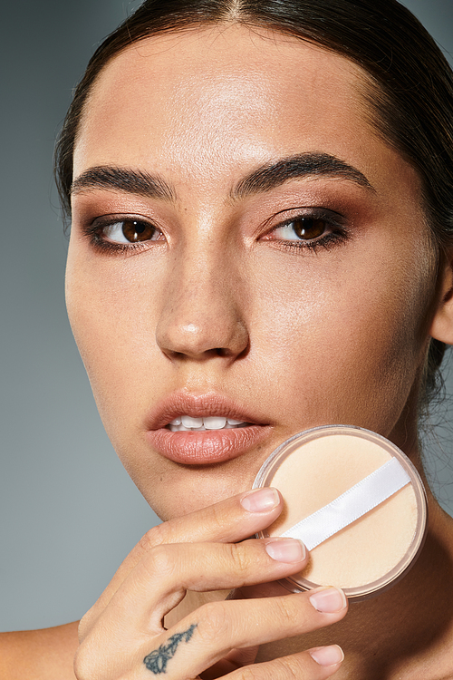 The beautiful woman carefully applies makeup with a powder compact under studio lighting.