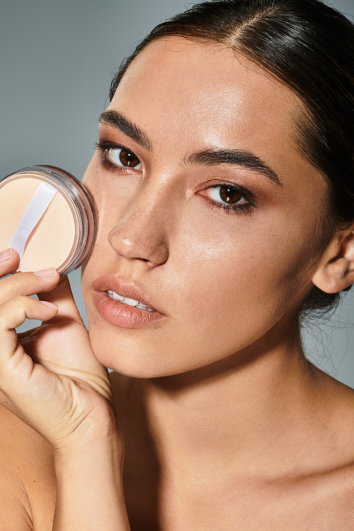 A striking woman with flawless skin applies makeup gracefully under studio lights.