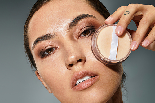 A beautiful woman enhances her features while holding a powder compact close to her face.