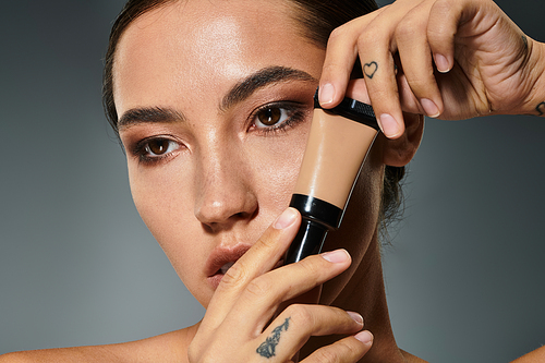 A stunning woman expertly applies foundation to enhance her natural beauty against a soft backdrop.