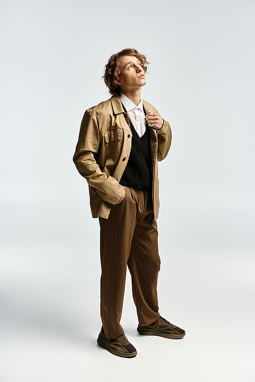 A handsome young man stands confidently in a chic autumn ensemble, exuding elegance in a studio.