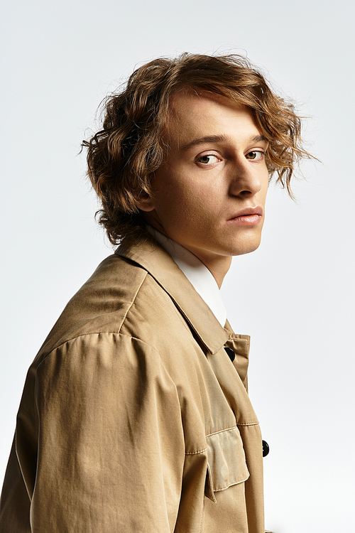 A handsome young man in a chic autumn outfit poses elegantly in a calm studio environment.