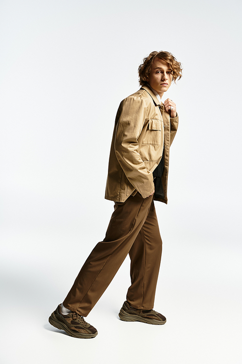 A striking young man displays his wavy hair and elegant autumn outfit in a contemporary studio.