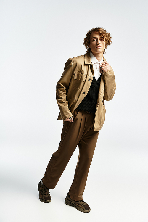 A handsome young man in a chic autumn outfit poses confidently in a minimalist studio space.