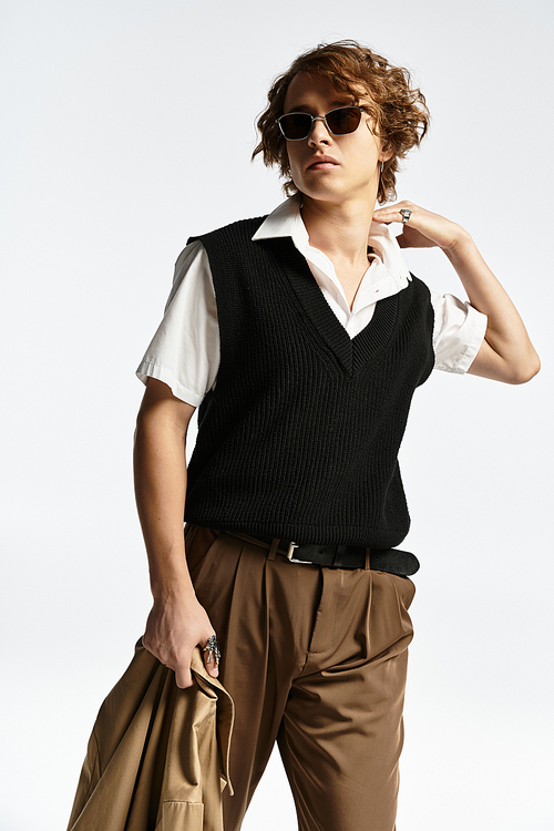 A handsome young man in a chic autumn outfit poses elegantly, highlighting his trendy style and wavy hair.