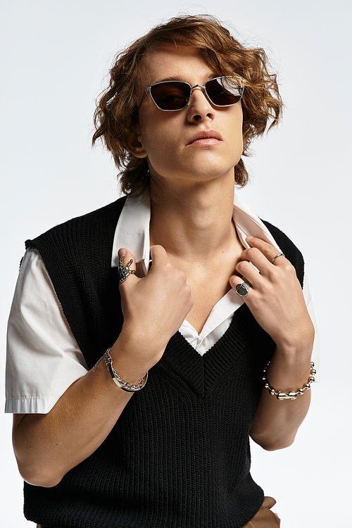 A handsome young man with wavy hair models an elegant autumn outfit, exuding confidence in a studio.