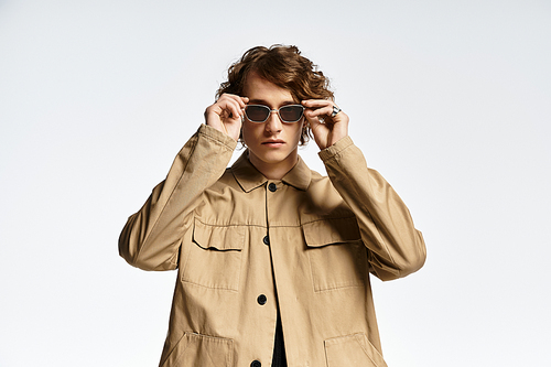 A handsome young man with wavy hair poses confidently, donning a chic autumn outfit in an elegant studio.