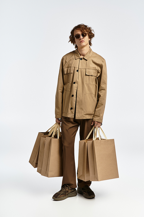 A handsome young man in an elegant autumn outfit stands confidently holding shopping bags.