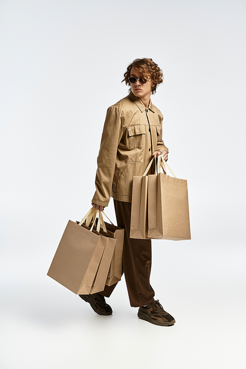 A handsome young man in a chic autumn outfit confidently carries shopping bags in a modern studio setting.