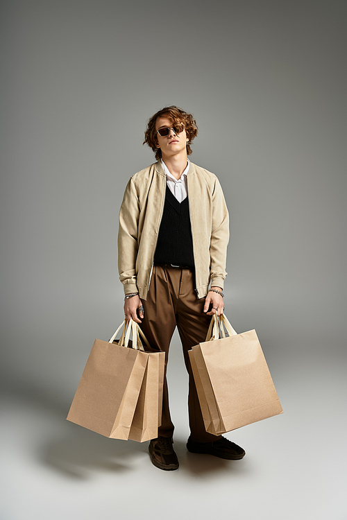 A dapper young man stands confidently with two shopping bags, showcasing elegant autumn attire in a studio.