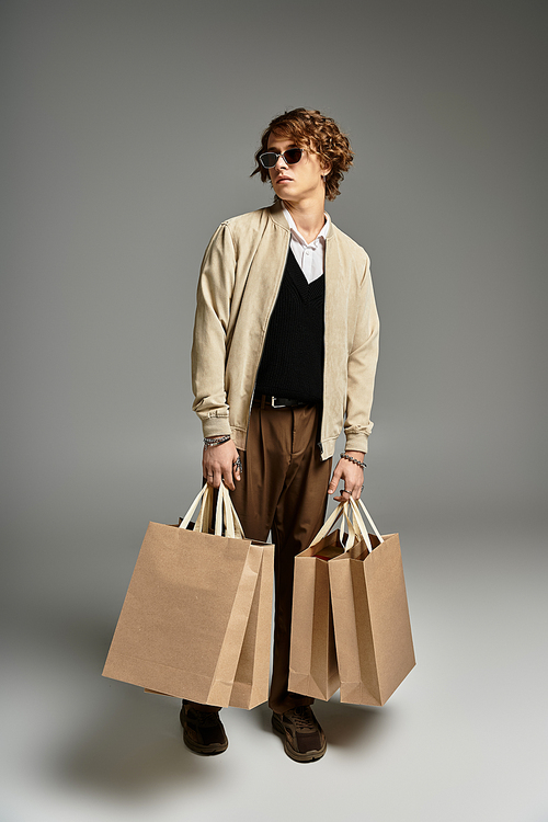 A fashionable young man stands tall in elegant autumn clothing, holding shopping bags with poise.