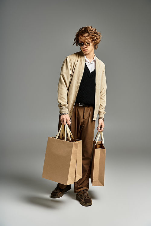 A handsome young man in an elegant autumn outfit holds shopping bags while posing in a stylish studio.