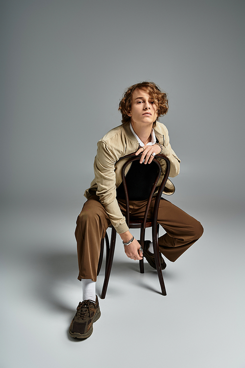 A handsome young man showcases his wavy hair and elegant autumn attire while posed against a neutral backdrop.