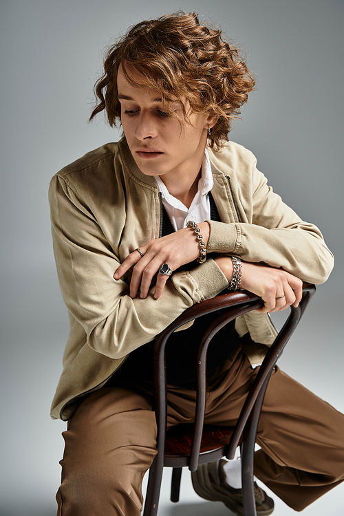 A handsome young man sits thoughtfully on a chair, dressed in elegant autumn fashion and showcasing his wavy hair.