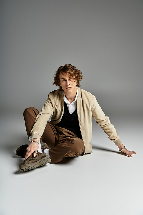 This young man with wavy hair elegantly poses in autumn attire within a contemporary studio.