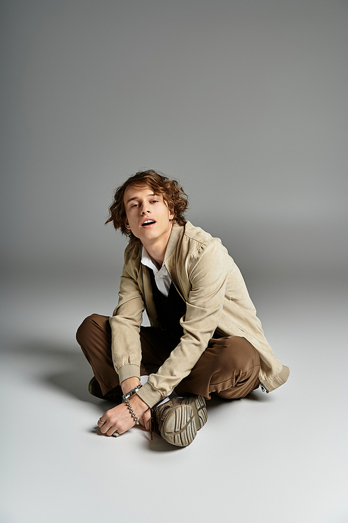 A handsome young man with wavy hair showcases a trendy autumn outfit while seated gracefully.