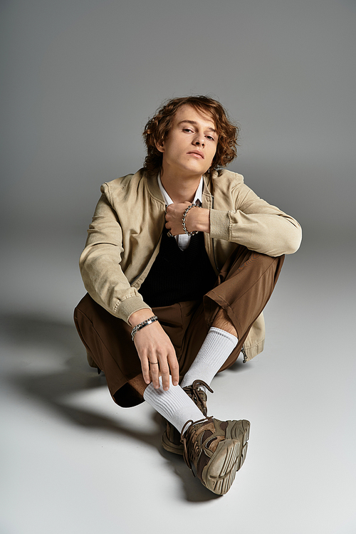 A handsome young man sits comfortably in a studio, showcasing his elegant autumn outfit with confidence.