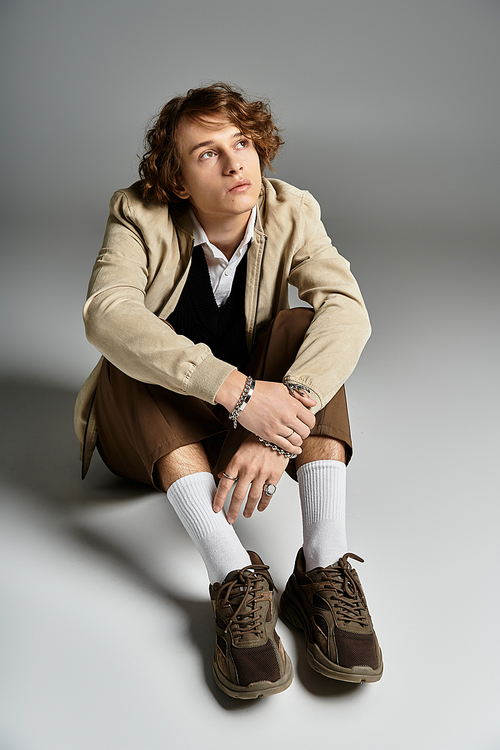 A handsome young man in a chic autumn outfit sits thoughtfully in a studio, showcasing his unique style.