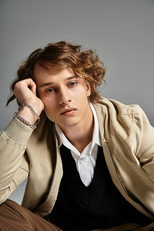 A handsome young man with wavy hair showcases an elegant autumn look while striking a contemplative pose.