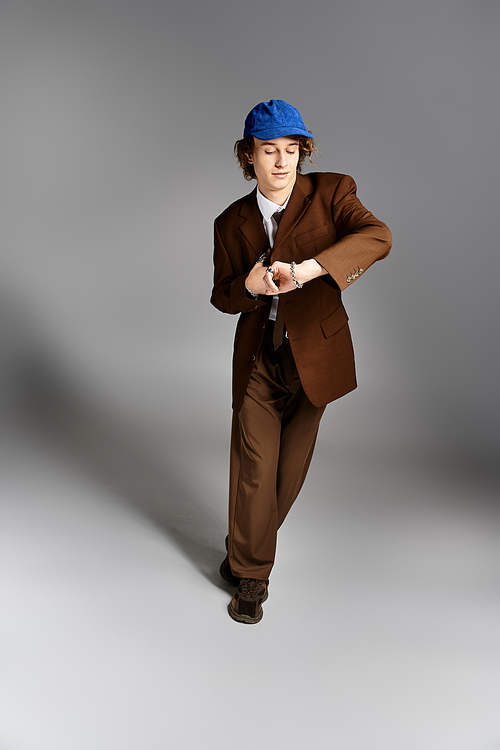 A dapper young man confidently poses in a brown suit and blue cap, showcasing his unique style in a studio.