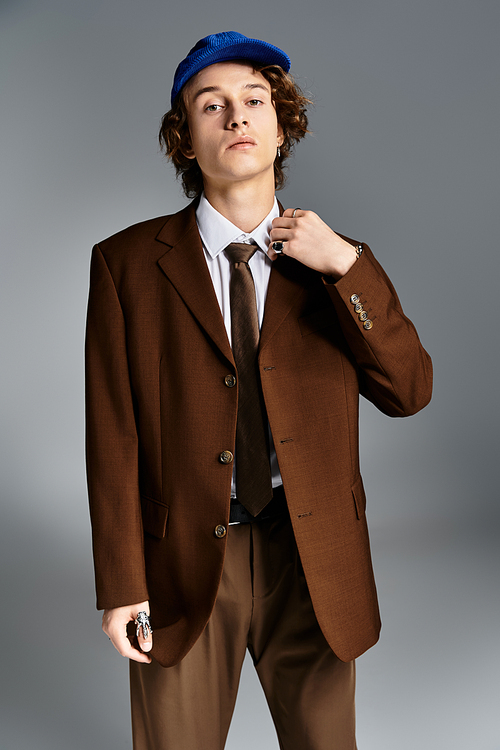 A fashionable young man stands tall in a brown suit and baseball cap, showcasing his unique style in a studio.