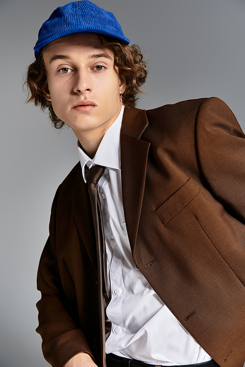 In a chic studio, a handsome young man dressed in a brown suit and baseball cap showcases a modern aesthetic.