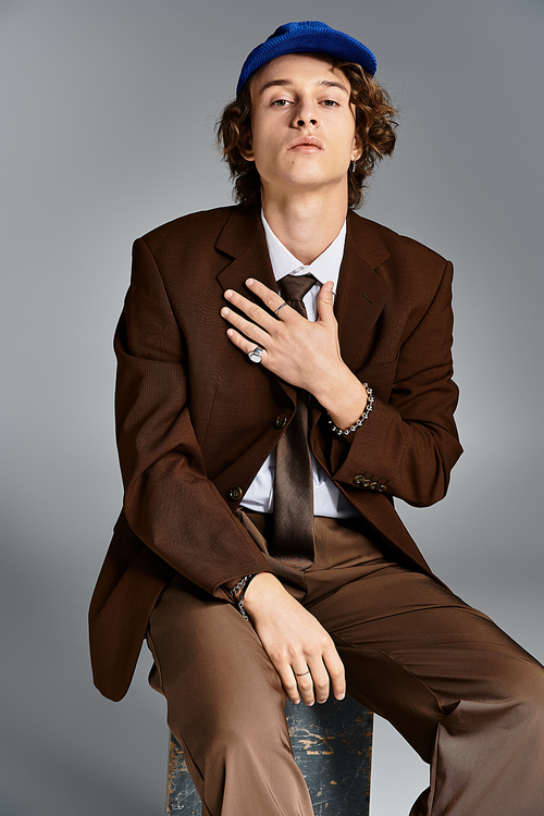 A handsome young man dressed in a brown suit and baseball cap expresses confidence while seated creatively.