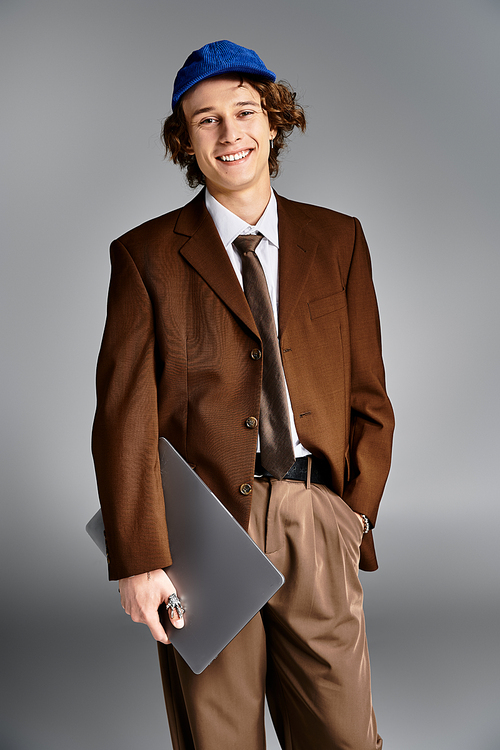 A young man with curly hair stands confidently in a brown suit, holding a laptop, showcasing his unique style.