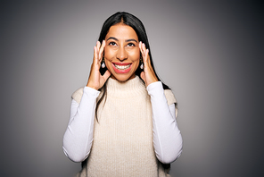 The young woman beams with happiness, hands on her face, surrounded by a warm background.