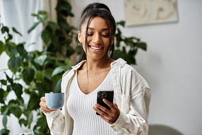 A cheerful young woman engages with her phone and sips coffee in her comfortable study space.