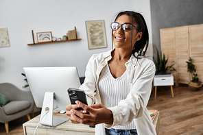 A cheerful young woman engages with her smartphone while studying in her cozy home workspace.